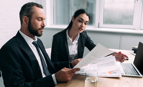 Business Man And Woman Looking At Paperwork With Laptop On Desk