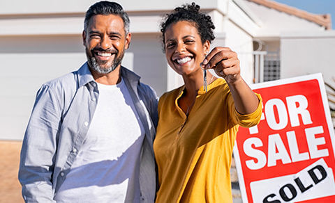 Couple Holding A House Key In Front Of A Home With A Sold Sign