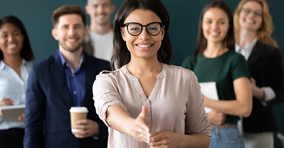 Woman Extending Her Hand For A Handsheke Wth Vrious People Standing Behind Her