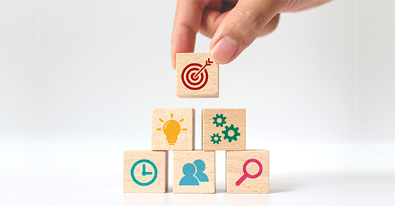 Hand Holding A Block Placing It On A Stack Of Wooden Blocs With Icons On Them