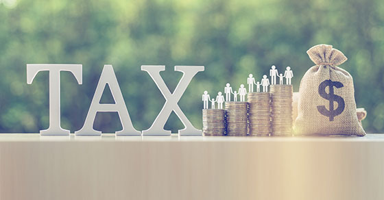 Block Letters Spelling Tax On A Wall Alongside Stacks Of Coins