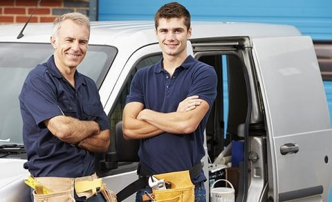 Father And Son Standing In Front Of A Van Wearing Tool Belts