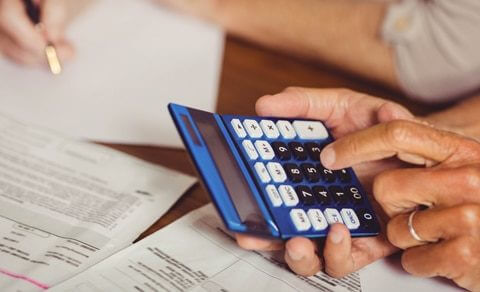 Close Up Of Male's Hands Holding A Calculator With Bills Underneath His Hands