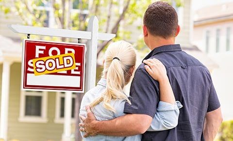 Couple Hugging Looking At A Home With A Sold Sign In Front Of It