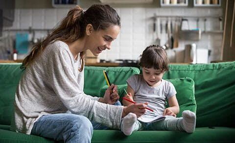 Mother Helping Her Toddler Daughter Color While Sitting On A Green Couch