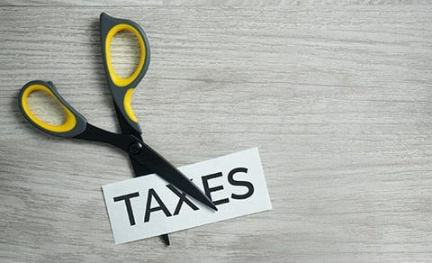 Pair Of Scissors Cutiing A Piece Of Paper In Half With The Word "taxes" On It