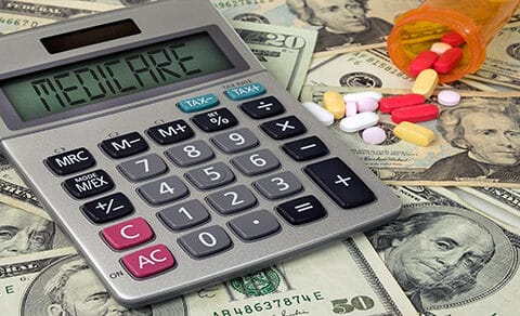 Calculator with read out MEDICAIRE on top of dollar bills next to a spilled bottle of pills