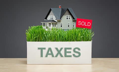 A box on a table with grass and a small model of a home in it with a sign that says sold.