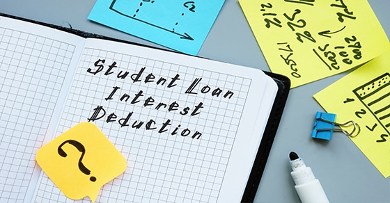 Notebook with the phrase Student Loan Interest Deduction written in it, post it with a question mark on the page. Various post its on desk surrounding it