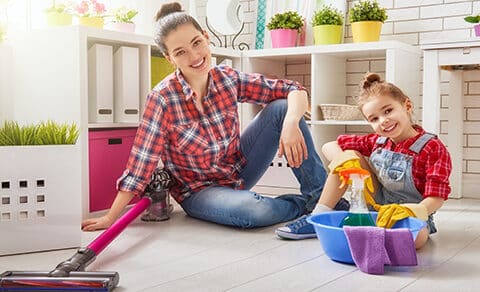 Nanny in a red plaid shirt and a child in overalls sitting on the floor of a home