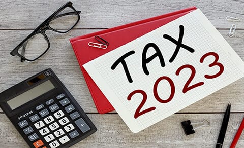 Desktop with calculator, reading glasses, pens and notepaper that says Tax 2023