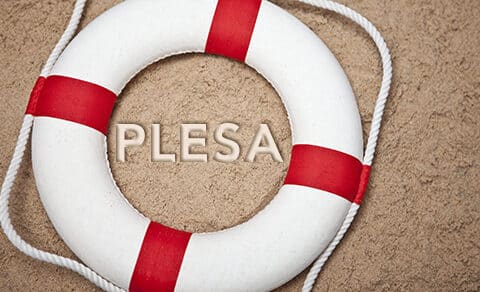 Red and white life saving ring on the sand with the word PLESA written in the sand
