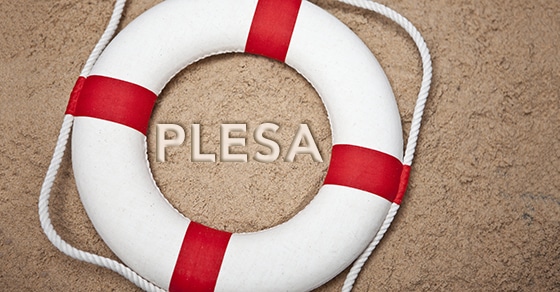 Red and white life saving ring on the sand with the word PLESA written in the sand