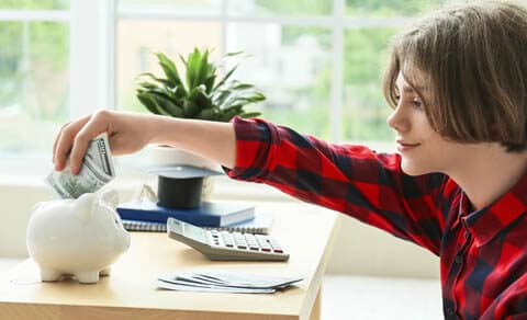 teen in a red and black flannel shirt putting money into a white piggy bank