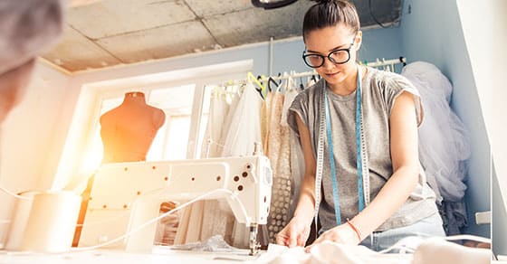 Woman who is a seamstress working on an article of clothimg with a sewing machine next to her