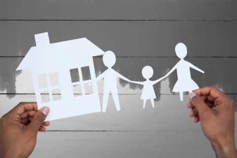 Two hands holding a paper doll cutout of a family and their house