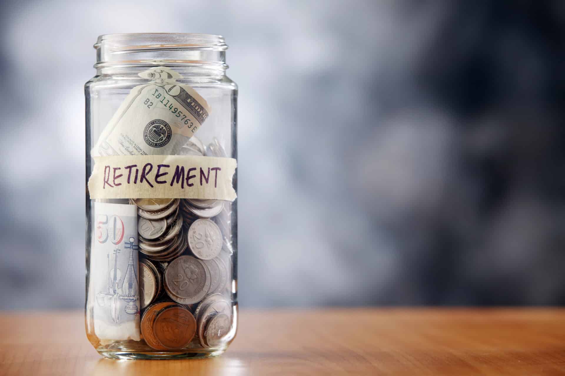 Glass jar filled with coins and a lable on it wit the word RETIREMENT, on a wooden table