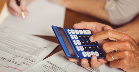 hand of a man holding a blue calculator resting on tax forms