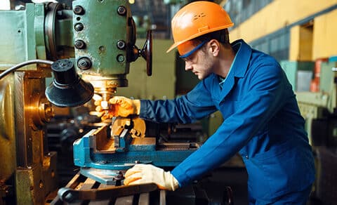 Male Technician ina bright blue jumsuit with an orange hard hat Works On Lathe, Plant
