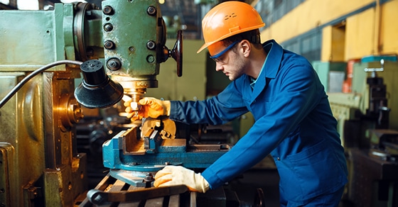 Male Technician ina bright blue jumsuit with an orange hard hat Works On Lathe, Plant