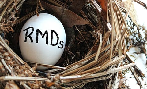 white egg, in a nest, with "RMDs," written on it, symbolizing retirement savings, and Required Minimum Distributions.