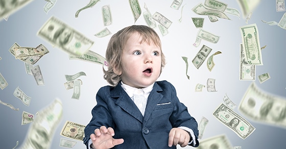 A, young, child, in, a, suit, looks, surprised, as, dollar, bills, rain, down, around, them, symbolizing, wealth, or, unexpected, financial, gains.