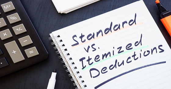 Notebook, handwritten text, "Standard vs. Itemized Deductions," calculator, marker, highlighter, dark surface, tax-related.