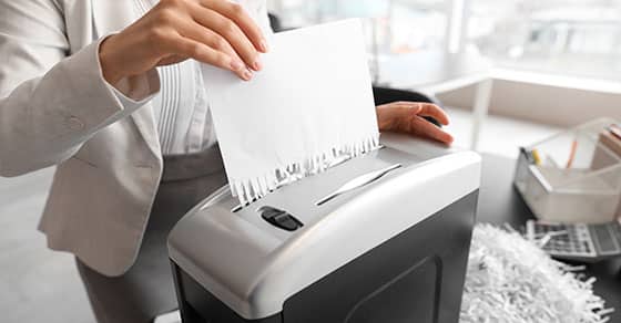 A, person, in, business, attire, is, shredding, a, document, using, an, office, paper, shredder, with, shredded, paper, visible, around, the, machine.