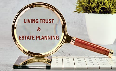 A, magnifying, glass, highlighting, the, words, "Living, Trust, &, Estate, Planning", placed, over, a, calculator, with, a, small, potted, plant, in, the, background, symbolizing, financial, planning, and, attention, to, detail.