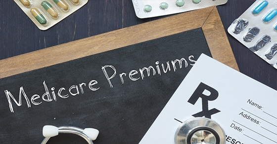 The, image, shows, a, chalkboard, with, "Medicare, Premiums", written, on, it, surrounded, by, pills, a, prescription, pad, and, a, stethoscope, highlighting, healthcare, costs.