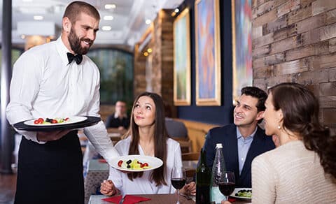 Waiter, serving, diners, restaurant, food, drinks, smiles, conversation, artwork, cozy.