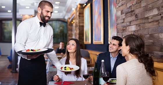 Waiter, serving, diners, restaurant, food, drinks, smiles, conversation, artwork, cozy.