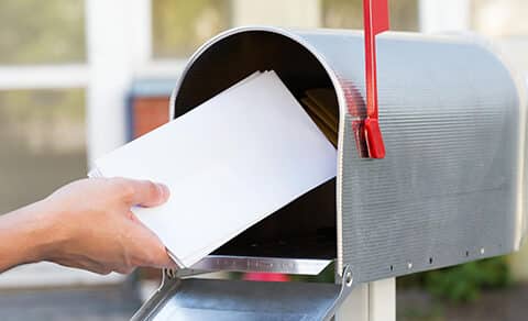 a, person, placing, white, envelopes, into, a, mailbox, with, the, red, flag, raised.