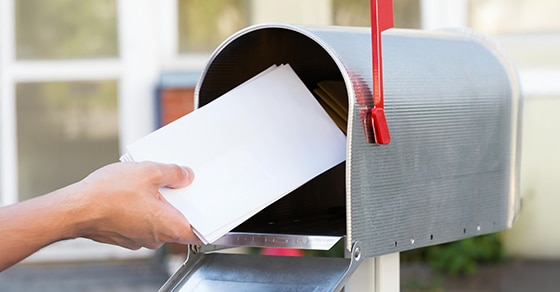 a, person, placing, white, envelopes, into, a, mailbox, with, the, red, flag, raised.