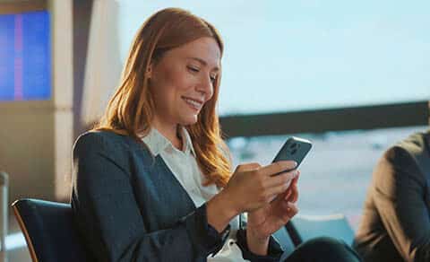 Smiling,businesswoman,using,mobile,phone,in,airport,lounge,,enjoying,comfortable