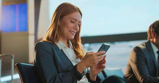 Smiling,businesswoman,using,mobile,phone,in,airport,lounge,,enjoying,comfortable